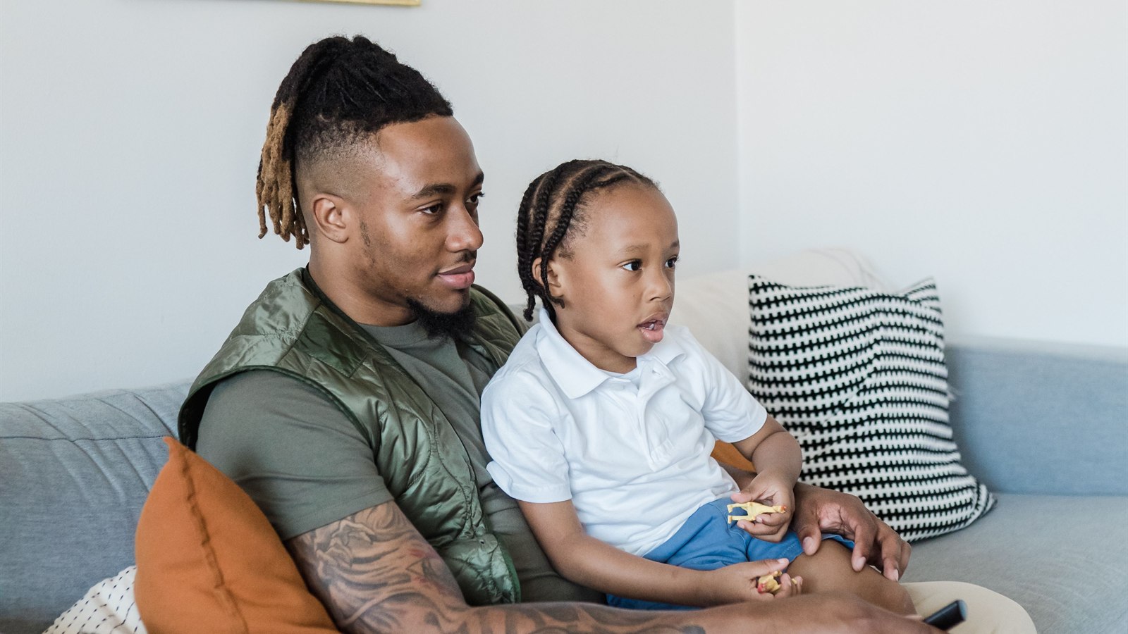 An adult and child sit closely together on a couch during a quiet moment at home