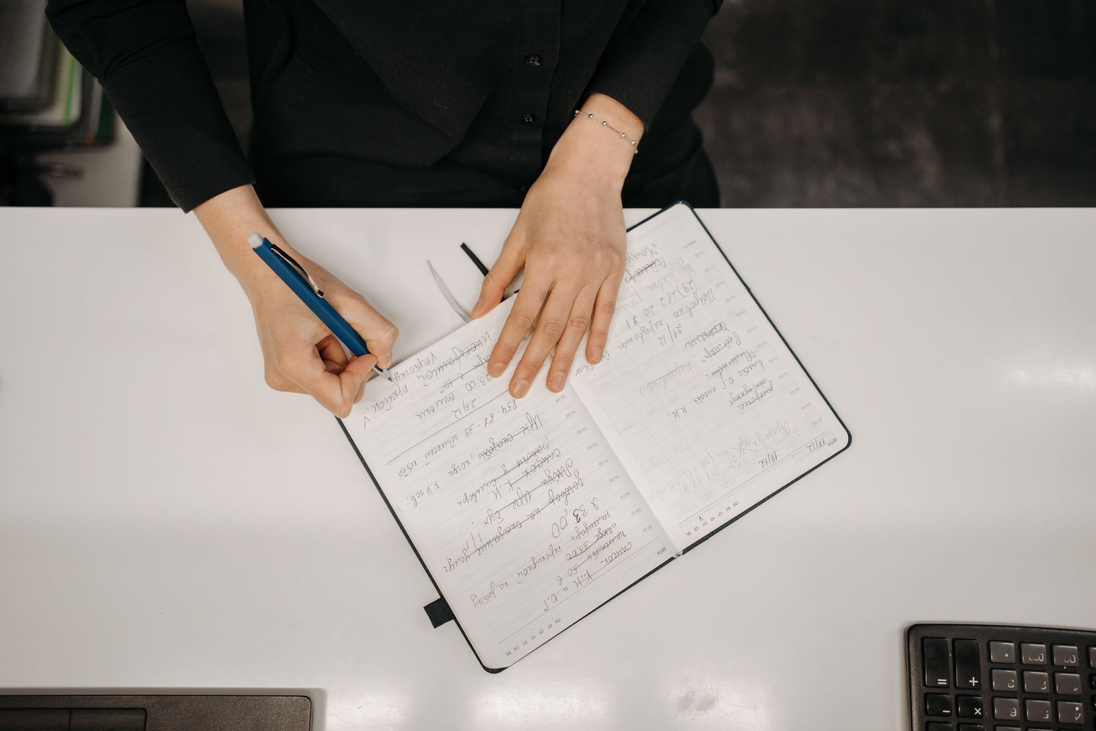 Adult hands writing notes in an open notebook on a white desk.
